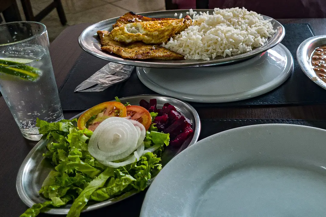 Prato feito com frango grelhado, ovo, arroz, feijão e salada servidos em travessas de alumínio